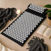Acupressure mat and pillow on a beige carpet with candles and a book in the background