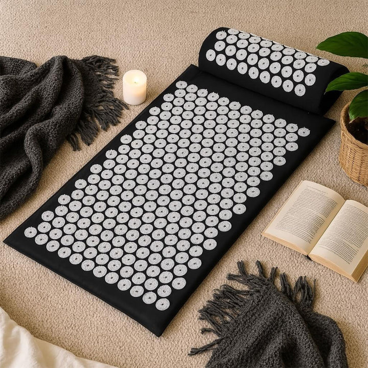 Acupressure mat and pillow on a beige carpet with candles and a book in the background